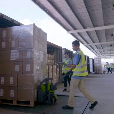 Worker moving palletized cartons at the factory loading dock.