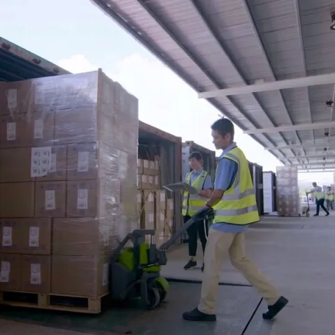 Worker moving palletized cartons at the factory loading dock.