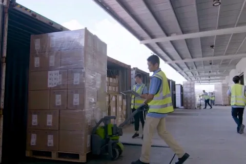 Worker moving palletized cartons at the factory loading dock.