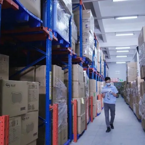 Warehouse aisle with tall storage racks and stacked cartons for product inventory.