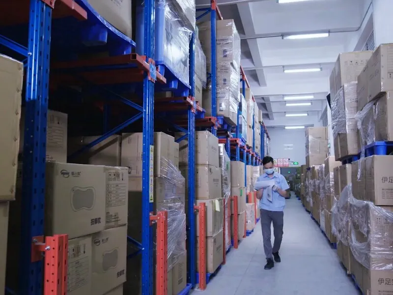 Warehouse aisle with tall storage racks and stacked cartons for product inventory.