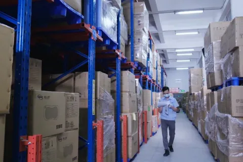 Warehouse aisle with tall storage racks and stacked cartons for product inventory.